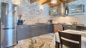 A modern kitchen with a stone wall, stainless steel appliances, and a dining area with a table and chairs. - Beautifull Istrian Villa Patrick with a pool (Pazin)