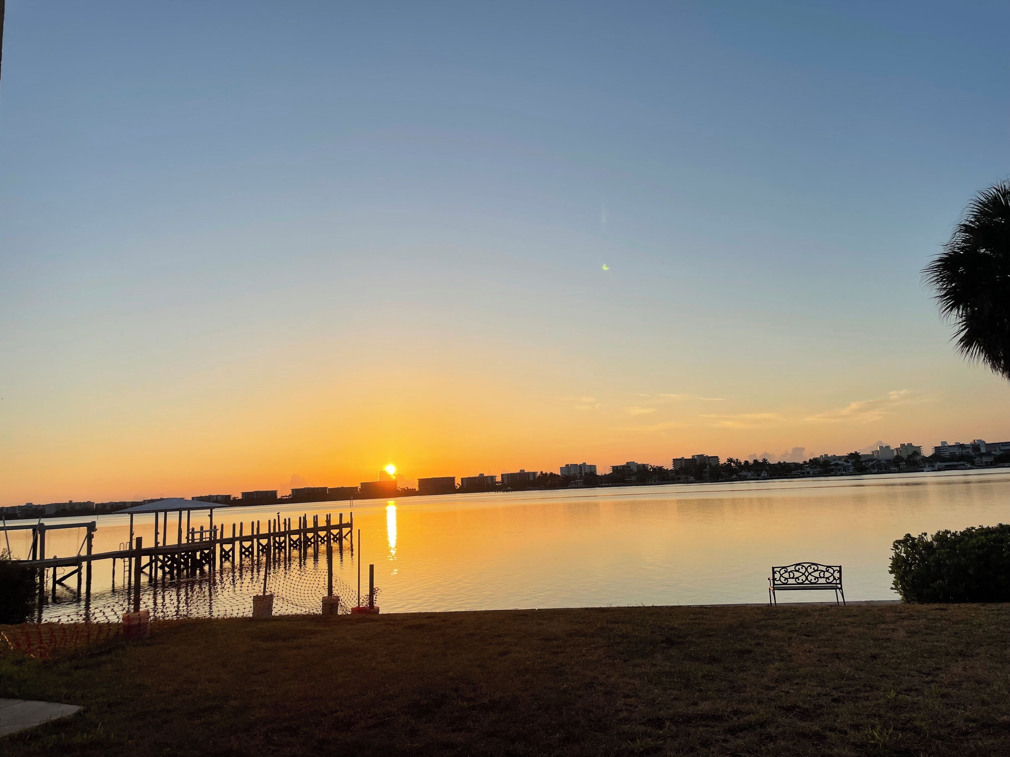A sunset over a calm lake with a dock and a bench in the foreground.