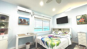 Un dormitorio con cama, escritorio, silla, televisor y ventana con persianas.