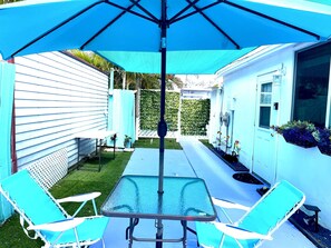 Eine Terrasse mit Tisch und Stühlen, einem blauen Sonnenschirm und einem weißen Zaun.