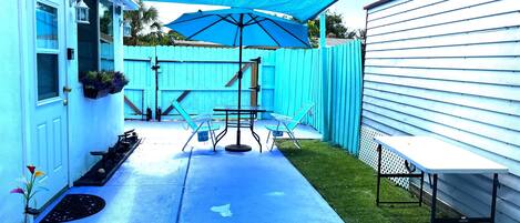 A backyard patio with a blue umbrella, a table, and chairs.