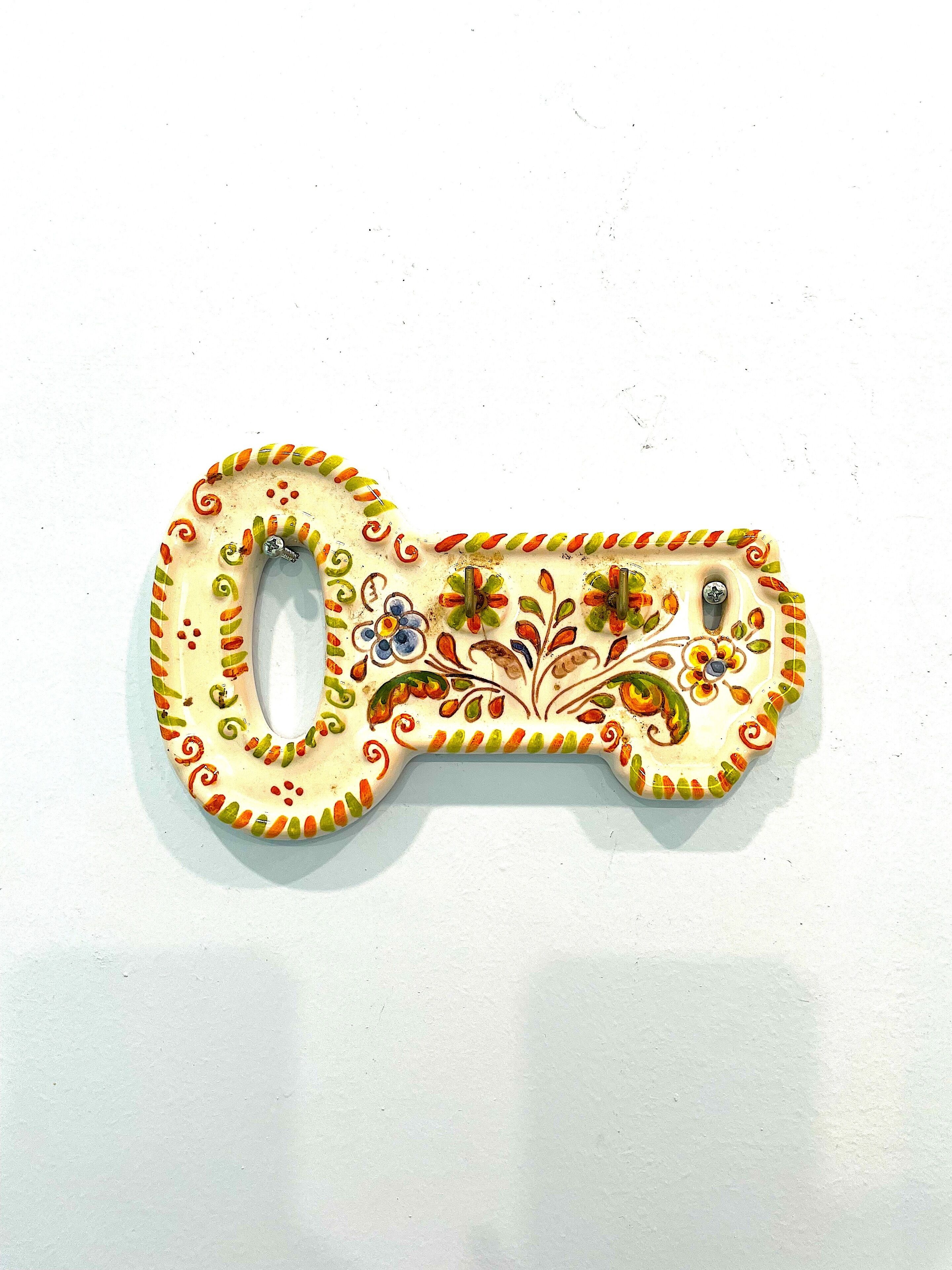 Un objet décoratif en forme de clé, orné de motifs floraux et doté d’un trou au centre.