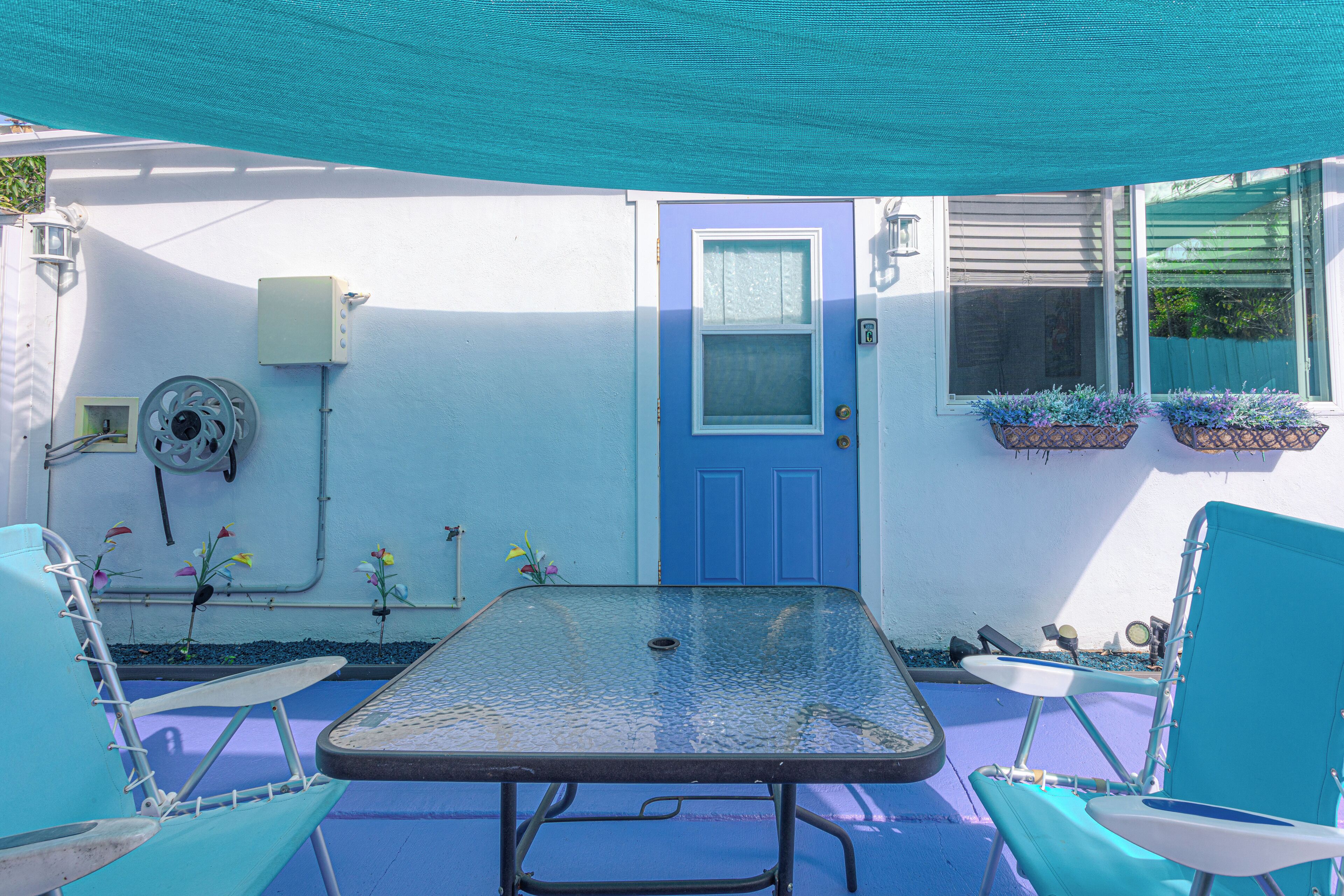 A patio with a table, chairs, a blue door, and flower planters.