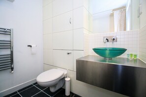 A modern bathroom with a white toilet, a stainless steel sink with a green basin, and a towel rack.