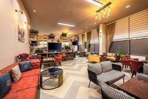 A modern living room with a sofa, armchairs, a coffee table, and a TV. There are shelves with plants and a fireplace. - Best Western Premier Hidden Hills (Arnavutköy)