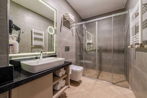 Casa de banho moderna com um espelho grande, uma pia, uma sanita e uma cabine de duche com portas de vidro.