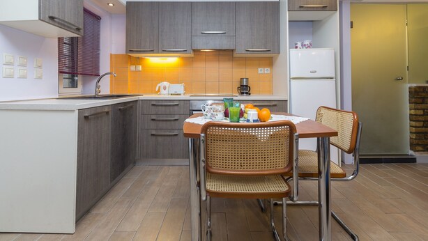 Une cuisine moderne avec des meubles de couleur grise, une table à manger en bois et deux chaises en osier.