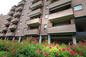 A multi-story residential building with balconies, brick exterior, and a garden with pink flowers. - UR-NEST Fantin, Modern and bright one-bedroom apartment  (Bologna)