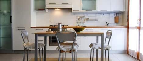 Cocina moderna con armarios blancos, encimera de madera y una isla central con un bol. Hay cuatro sillas alrededor de la isla.