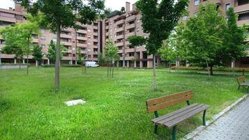 Un'area verde con prato, una panchina e alberi, circondata da edifici residenziali.
