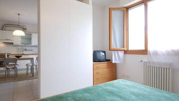 Una camera da letto con un letto, una cassettiera, una televisione e una finestra con tende.