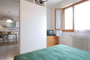 A bedroom with a bed, a dresser, a television, and a window with curtains.
