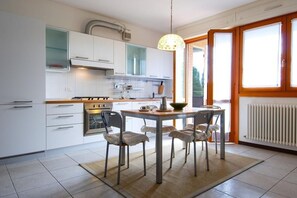 A modern kitchen with white cabinets, a gas stove, and a dining area with chairs and a table. - UR-NEST Fantin, Modern and bright one-bedroom apartment  (Bologna)