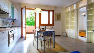 Una cucina moderna con mobili bianchi, un'area pranzo con tavolo e sedie, e un'ampia finestra che offre luce naturale.