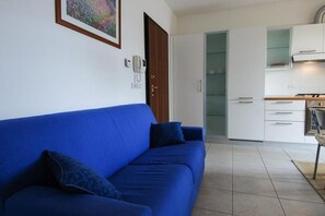 A living room with a blue sofa, a door, and a kitchen area with white cabinets and a stove.