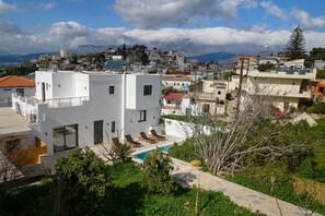 A modern white building with a rooftop pool and lounge chairs.
