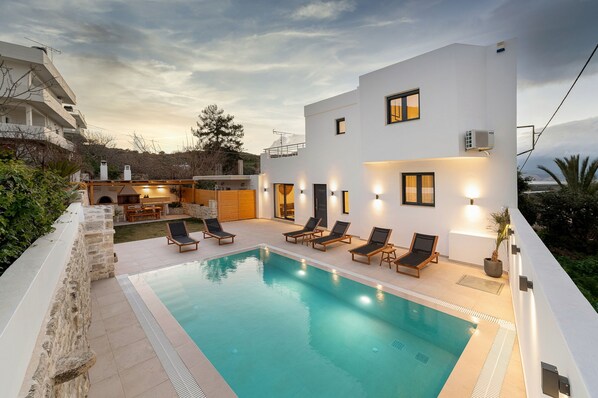 A modern house with a swimming pool, outdoor seating, and a view of the surrounding landscape.