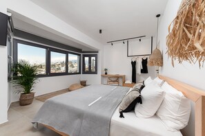 A modern bedroom with a large bed, a desk, a hanging plant, and a view of the city through large windows.