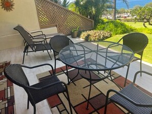 A patio with a round glass table and six chairs, surrounded by a patterned rug and a lattice fence.