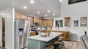 A modern kitchen with wooden cabinets, stainless steel appliances, a granite countertop, and bar stools.