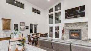 A modern kitchen with a granite countertop, a dining area with a wooden table and chairs, a built-in fireplace, and a large window overlooking the backyard.
