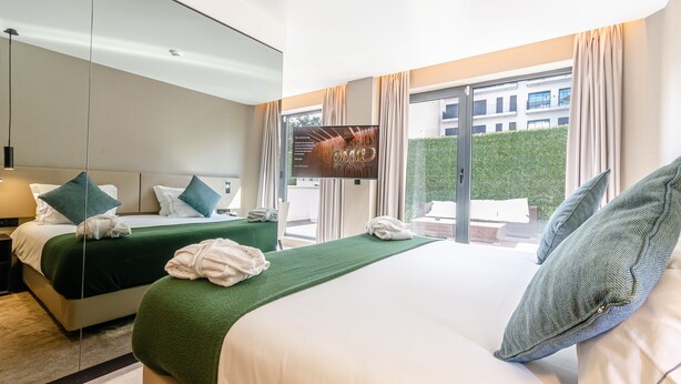Une chambre d’hôtel avec deux lits, une télévision, un téléphone et une vue sur un immeuble par la fenêtre.