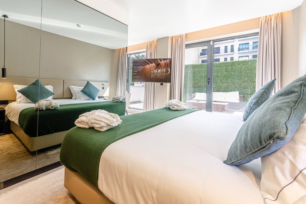 Ein Hotelzimmer mit zwei Betten, einem Fernseher, einem Telefon und Blick auf ein Gebäude durch das Fenster.