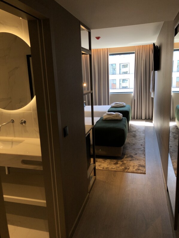 Habitación de hotel con cama, un pequeño sofá, baño con bañera y ventana con cortinas.