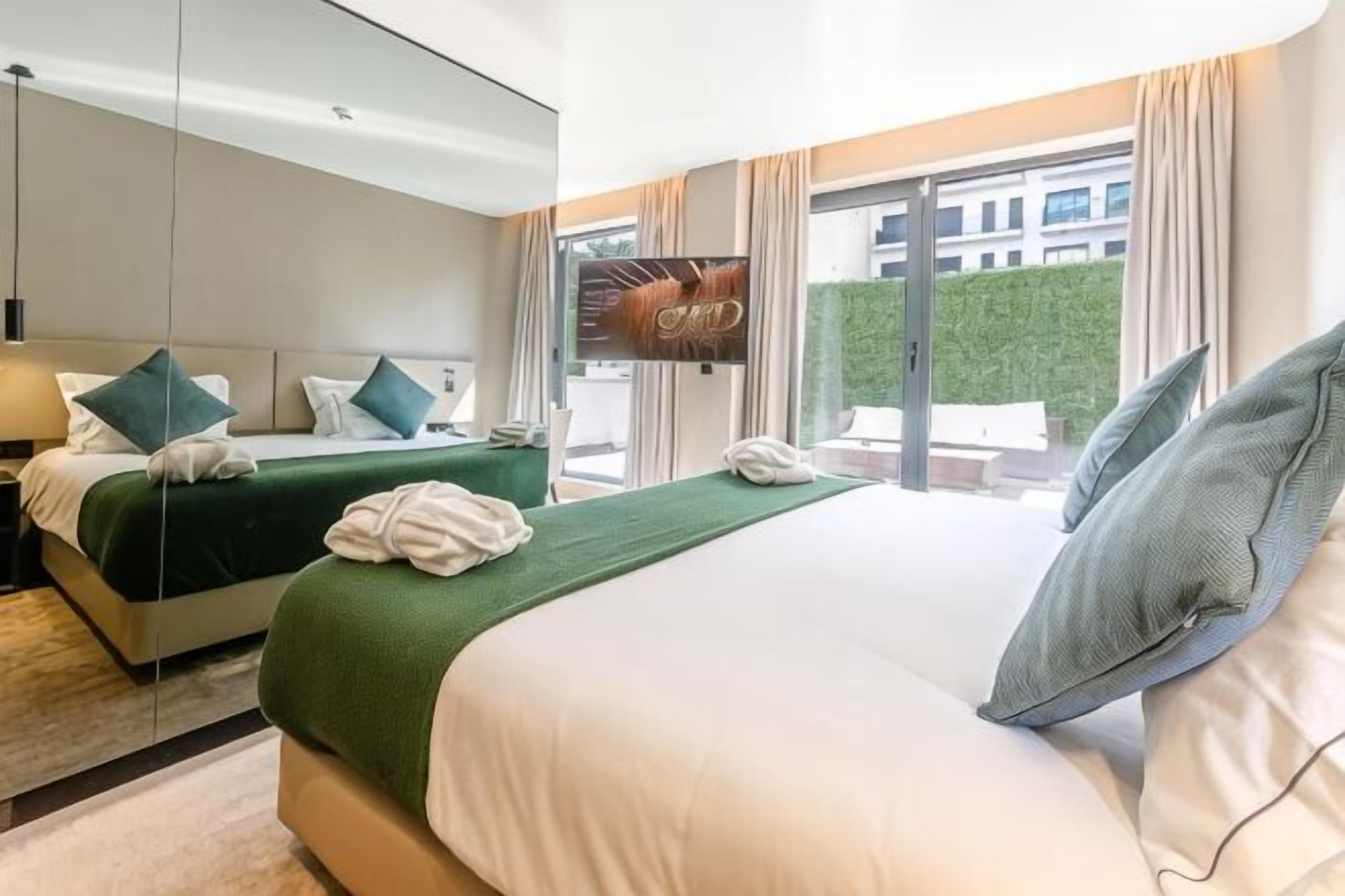 Hotellihuone, jossa on kaksi sänkyä, televisio ja näkymä rakennukseen ja viheralueille.