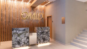 Un espace d'accueil au design moderne, avec un mur à lattes de bois, un comptoir d'accueil en marbre et un escalier situé sur la droite.