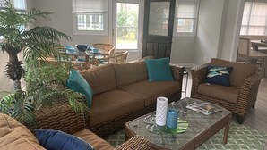 Un salón acogedor con un sofá seccional marrón, sillones de mimbre y una mesa de centro de cristal.
