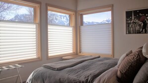 Una camera da letto con un letto grande, tre finestre con tende, un tavolino e un quadro appeso al muro.