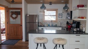 Una cucina moderna con frigorifero in acciaio inossidabile, forno integrato e lavello. Due sgabelli da bar con sedute imbottite e una finestra sopra il lavello.