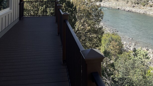 Una terrazza in legno con ringhiera che si affaccia su un fiume e montagne.