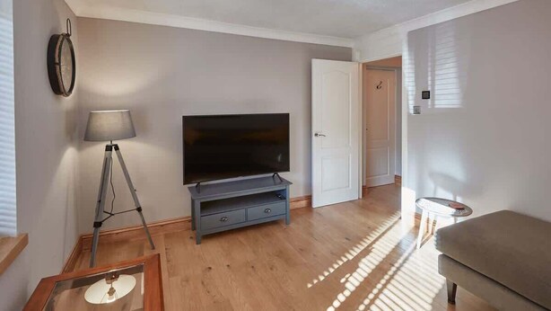 En stue med et fladskærms-tv på et stativ, en lampe og en sofa.