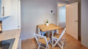 Et lille køkken med et træbord og hvide stole, en potteplante og en hvid dør.