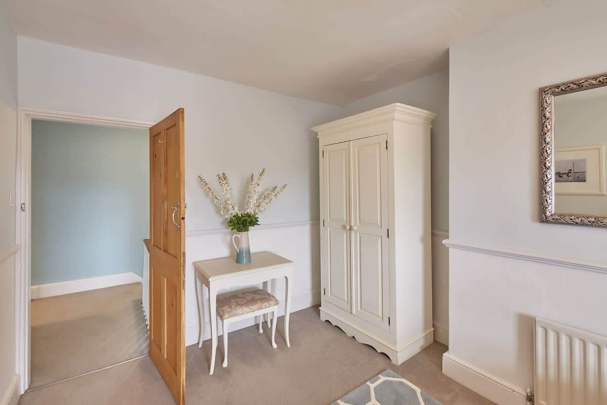 A hallway with a white door, a small table with a vase of flowers, a white cabinet, and a mirror on the wall.