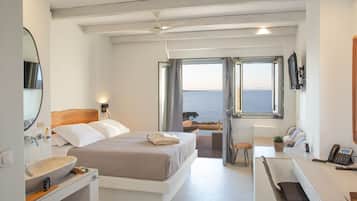 A modern hotel room with a large bed, a desk, a view of the sea, and a bathroom with a large mirror and sink.