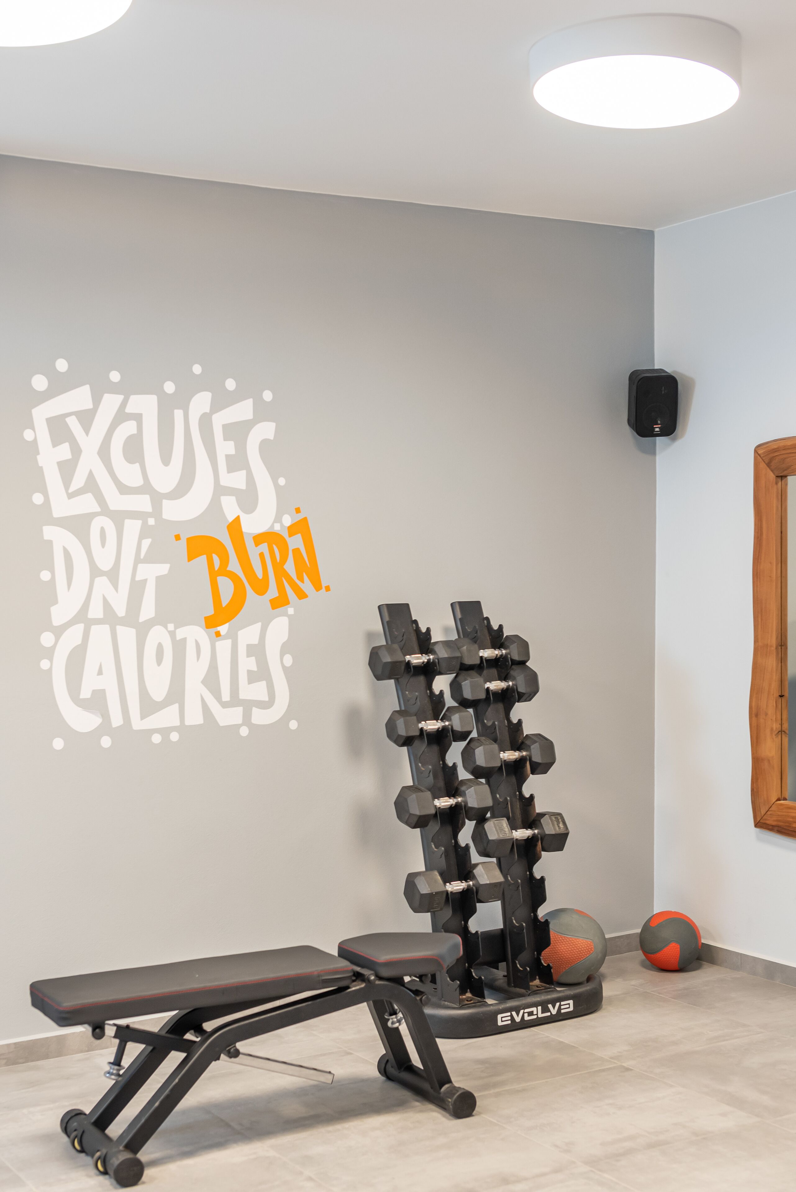 Uma academia com uma frase motivacional na parede, um banco, um suporte para halteres e bolas de exercício.