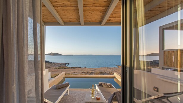 Un balcón con vista al mar, una piscina y sillas de descanso.