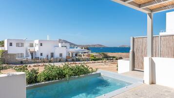 Um edifício branco moderno com piscina, rodeado por vegetação e vista para o mar.