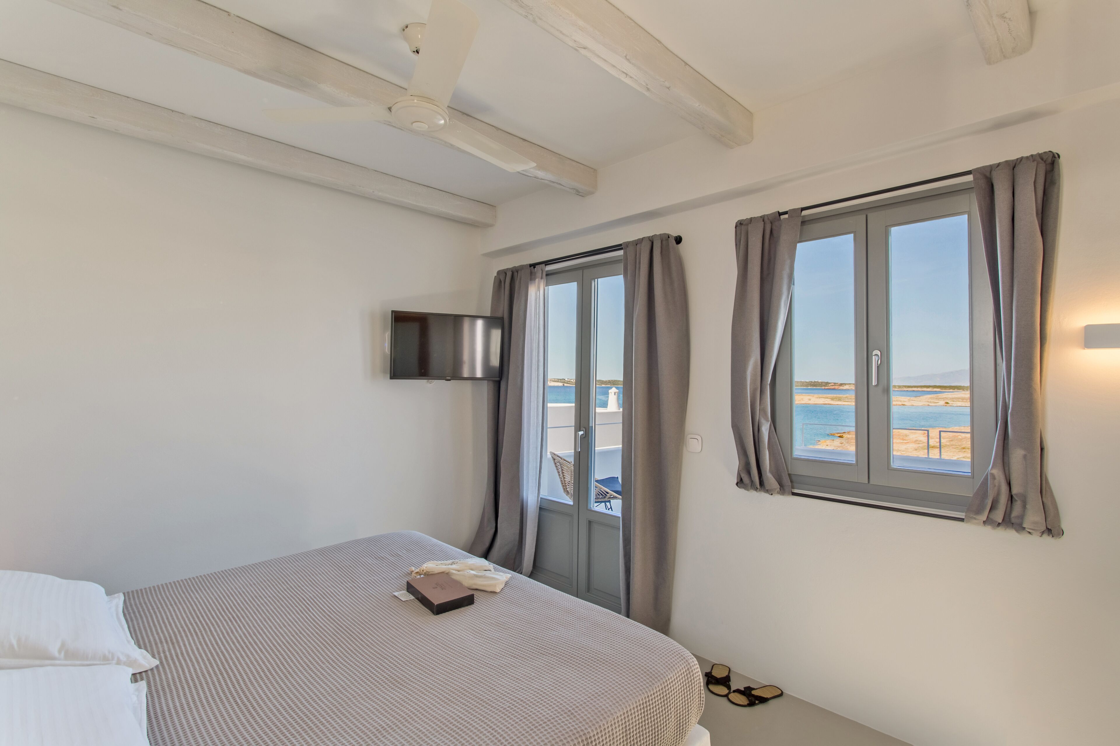 A bedroom with a bed, a TV mounted on the wall, and a window with curtains.