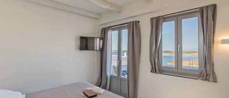 A bedroom with a bed, a TV mounted on the wall, and a window with curtains.