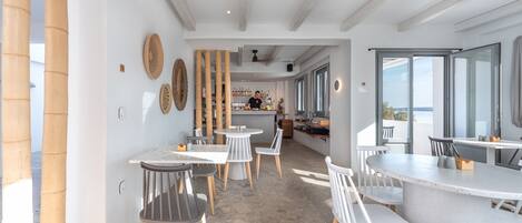 A modern dining area with white tables and chairs, bamboo decor, and a view of the kitchen in the background.
