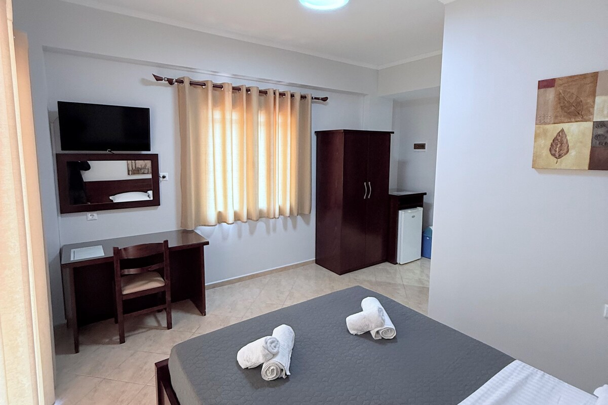 Habitación de hotel con cama, escritorio, silla, televisor, armario y baño.