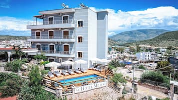 Ein mehrstöckiges Hotel mit Dachpool, Balkonen und Blick auf die umliegende Stadt und Berge.