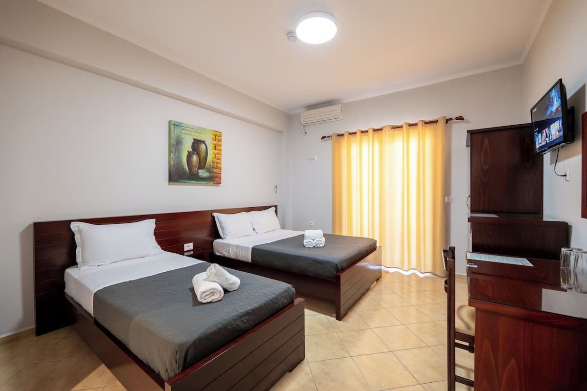 A hotel room with two beds, a wooden headboard, a flat-screen TV, a poster on the wall, and a window with curtains.