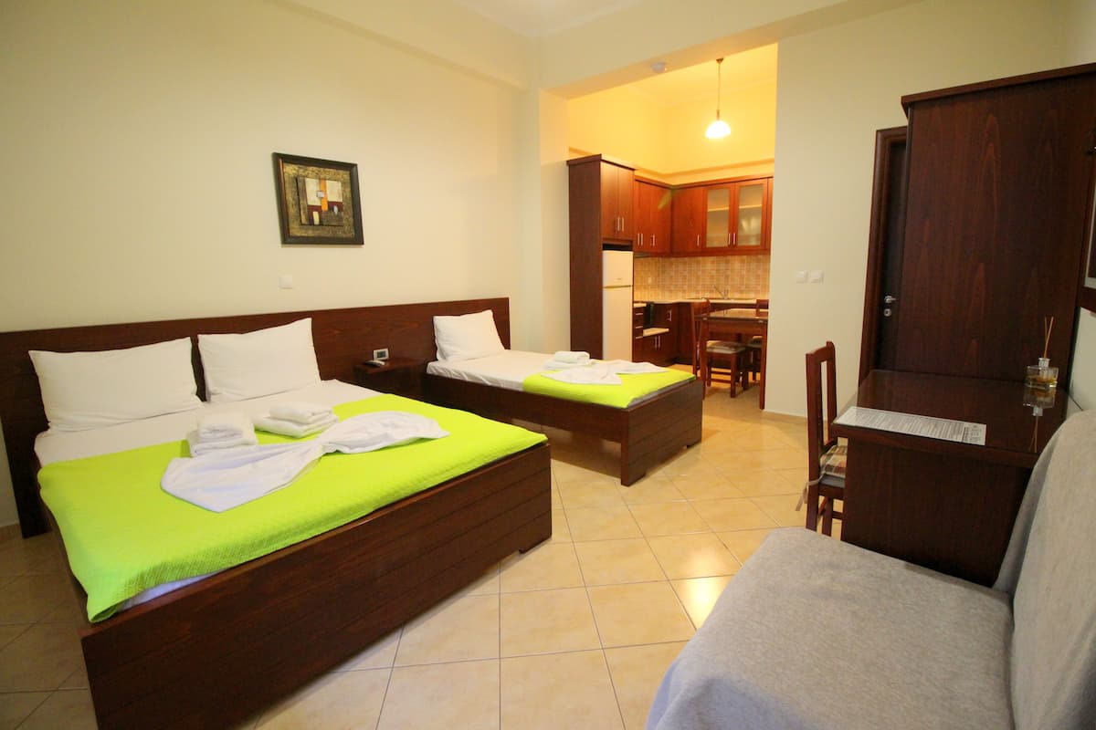 A hotel room with two beds, a sofa, a dining area, and a kitchen.