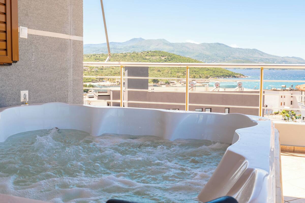 A hot tub on a wooden deck with a view of the sea and mountains.