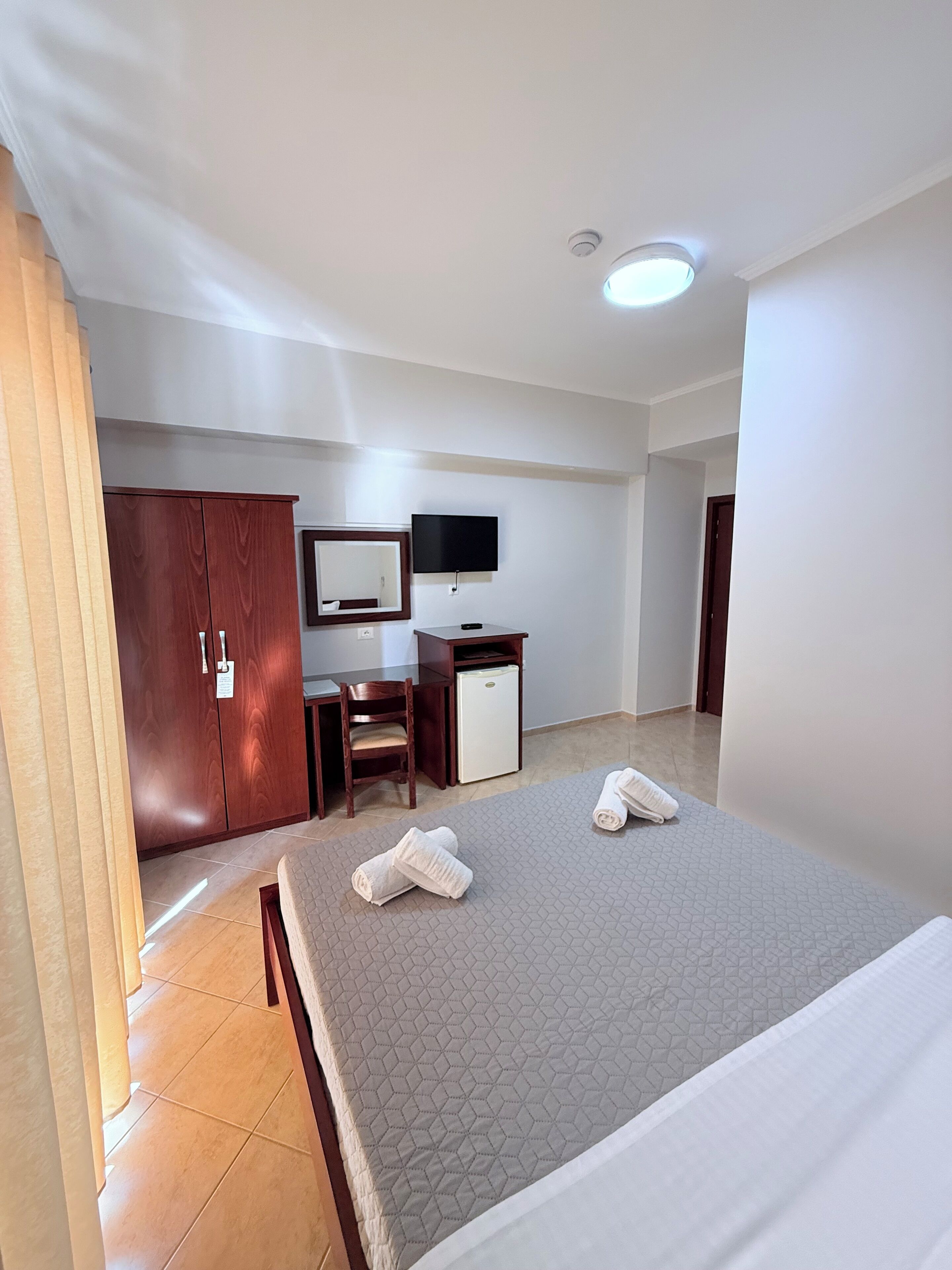 Una habitación de hotel con cama, escritorio, silla, televisor y armario.